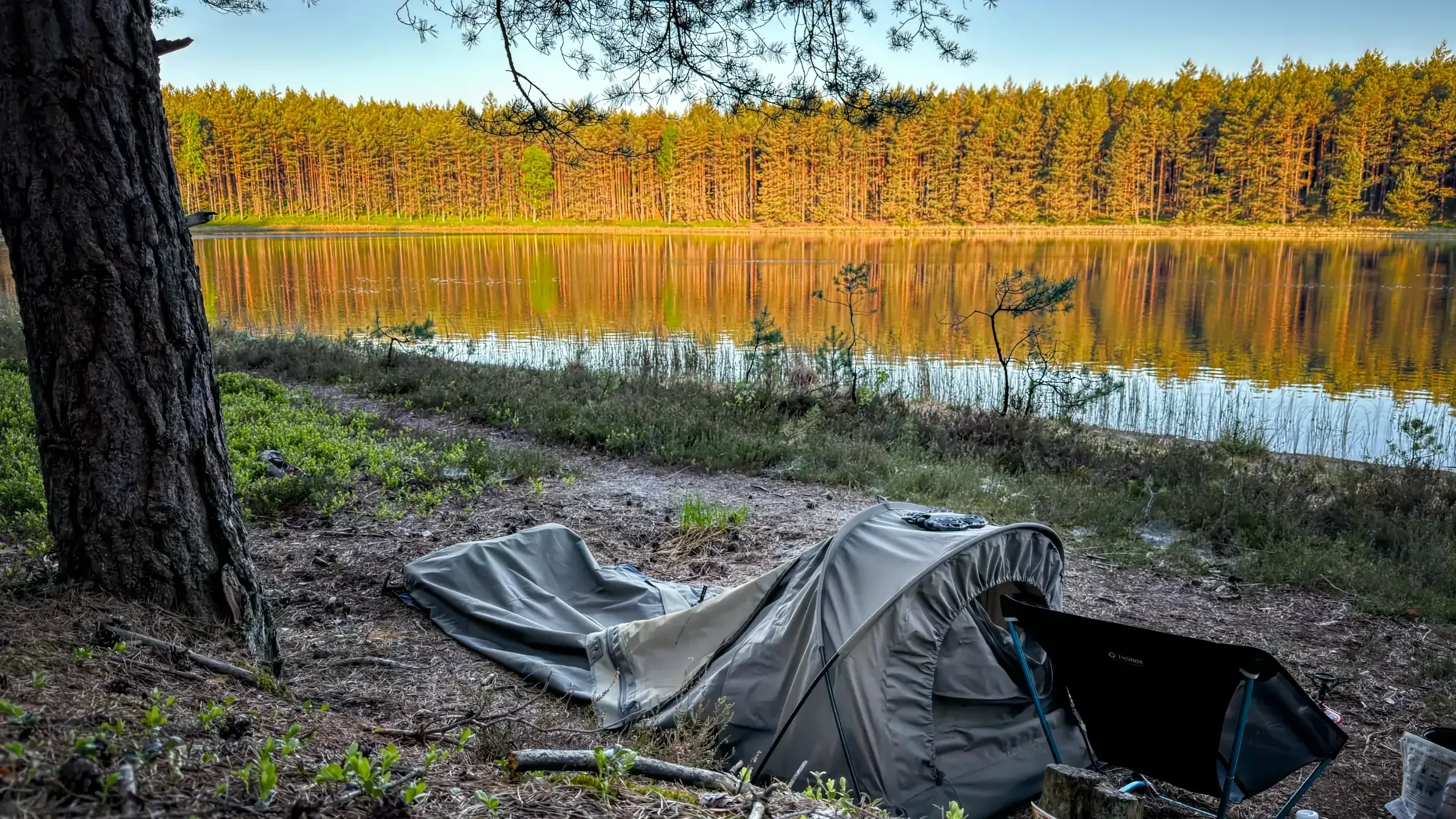 Carinthia Observer Plus Bivi Bag rozłożony nad jeziorem o wschodzie słońca.