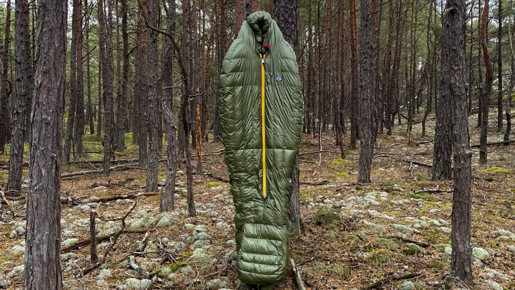 Prototypowy śpiwór Cumulus zawieszony pionowo między drzewami.