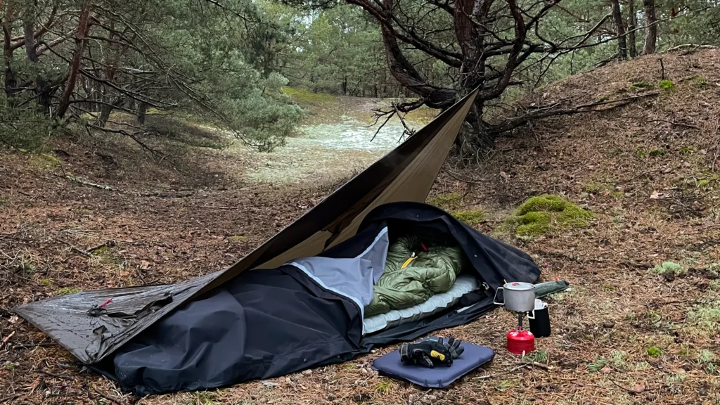 Bivi bag z pałąkiem rozłożony pod tarpem podczas biwaku w lesie.
