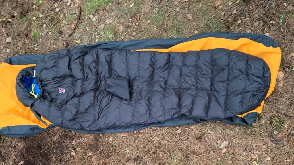 Śpiwór Fjällräven Move In Bag rozłożony na ziemi w lesie.