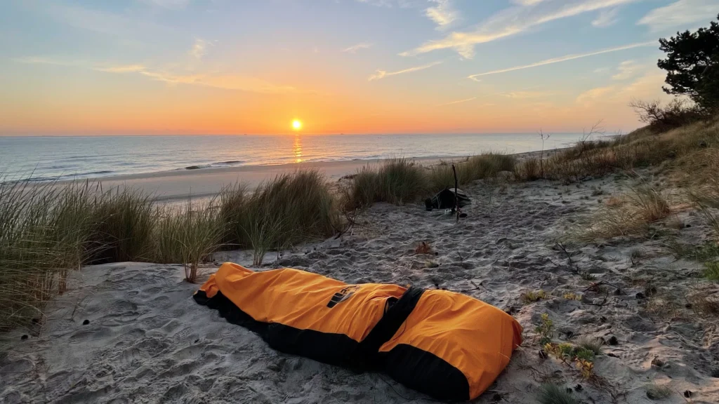 The North Face Assault Bivi rozłożony na plaży o zachodzie słońca.